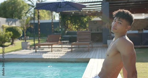 African American man in trunks noticing camera, turning from recline to smiling at pool, copy space