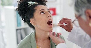 Healthcare, doctor and checking for tonsils with medical instrument in hospital. Wellness, otolaryngology and physician, dentist or ent specialist examining throat of a black woman for oral cancer.