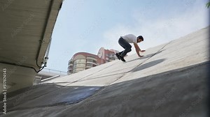 Male athlete jumps on a slope and slides down on a bright sunny day. Guy performs a parkour trick. Slow motion.