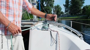 Skilled yachtsman shows young crew members how to use manual winch. Mariner shares experience explaining valuable technique