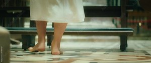Barefoot woman walking in church along the pews. Adult girl in a long dress praying on her knees. Close-up of feet.