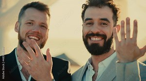 Portrait of a Happy Just Married Handsome Gay Couple in Love Showing Off Their Gold Wedding Rings. Two Attractive Queer Men in Suits Smile and Pose for Camera. LGBTQ Relationship and Family Goals.