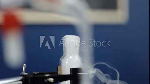 In a methodical slow-motion closeup, a test tube reveals a distinct chemical reaction, as white vapors ascend, epitomizing the precision and complexity of laboratory research