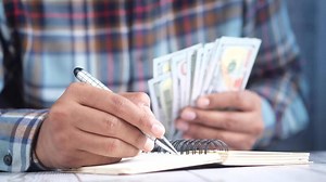 Man writing notes with pen and money on wooden table