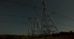 Nighttime view of high voltage power lines against the backdrop of moving stars in the night sky on a moonlit night. Concept of electricity and energy generation
