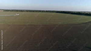 Crop Duster flies over field with wheat and splashing chemicals against parasite in drone view of vintage propelled plane flies beautifully over green plantation