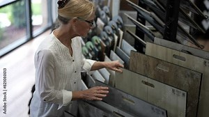 Happy mature woman shopping for flooring for home renovation redecorating project feeling the engineered tile sample in a showroom.