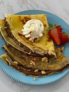 Soft, warm crepes filled with gooey Nutella—need we say more? 😍🍫 Perfect for breakfast or dessert, these are impossible to resist! 🥞✨ INGREDIENTS FOR 14 CREPES OF 18 CM DIAMETER Medium-sized eggs 3 All-purpose flour 250 g Whole milk 500 g Butter 40 g FOR GREASING THE PAN Butter as needed FOR FILLING AND GARNISHING Nutella 420 g Hazelnuts as needed Whipped cream as needed Strawberries as needed PREPARATION To prepare sweet and savory crepes, start by gently melting the butter in a saucepan. Le