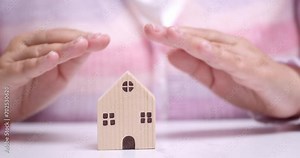 Hand covers the house. Home security concept, real estate insurance. Affordable housing. Realtor service. Inviolability of private property. Preservation of the cultural architectural fund.