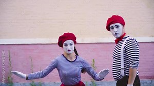 Two mimes dance near wall of building