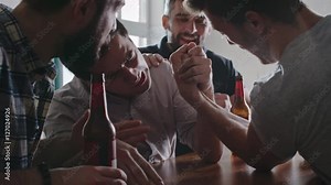 Asian man arm wrestling his friend at party while their mates cheering and laughing