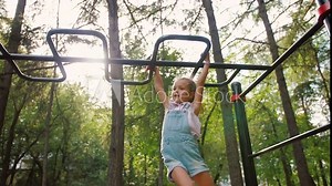 Little girl hanging and climbing on monkey bars in park on workout playground