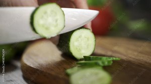 Hand Cuts Cucumber Rings CloseUp. Hands slicing fresh cucumber on a wooden cutting board.