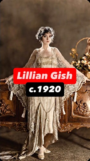 Lillian Gish, photographed around circa 1920, appears here in a theatrical studio portrait that emphasizes movement, delicacy, and emotional expression. She wears a flowing, translucent gown with lace sleeves, posed barefoot with arms extended, creating a soft, almost ethereal silhouette against the formal studio setting. By this time, Lillian Gish was already one of the defining faces of silent cinema, known for her collaborations with D. W. Griffith and her ability to convey deep emotion witho