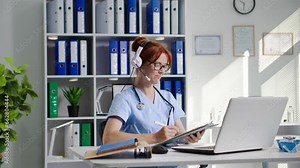 laboratory online, charming female medical laboratory assistant with a headset communicates with doctor via video call on laptop and shows reaction of reagents in test tube while sitting in medical
