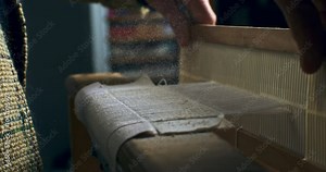 Super slow motion close of artisan touching threads with flying dust or talc powder particles splashing around, while working with woven weaving machine to craft cloth piece in workshop at 1000 fps.