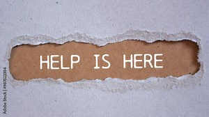 Help is here message writing on ripped torn paper on brown background. Conceptual help is here symbol.