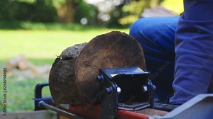 Close up of man using log splitting machine successfully and also getting splinter. Wearing jeans and blue jumper.
