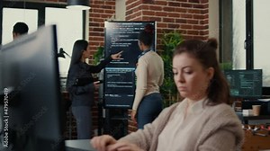 Software engineers analyzing code on wall screen tv looking for bugs and errors while colleague programer typing sitting at desk. App developers working on online cloud computing group project.