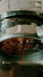 4K Pouring coffee stream from professional machine in cup. Barista man making double espresso, using filter holder. Flowing fresh ground coffee. Drinking roasted black coffee in the morning.