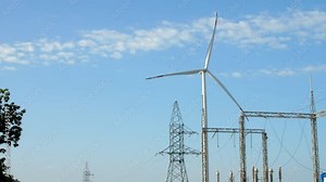 Wind turbine generates renewable energy against blue sky. Powerful propeller rotates near high grid tower and power lines at transformer substation