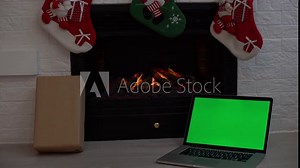 Home working notebook with Christmas background . Green screen of laptop. holiday business time. Home workplace near fireplace