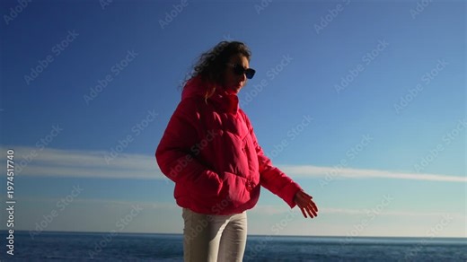 Woman puffer jacket ocean side view of a young woman standing by the sea wearing a bright pink coat on a windy day