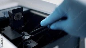 Scientist in blue gloves, putting a sample under a microscope.
