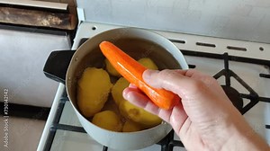 Man takes out and holds in his hand carrot from a pan with peeled potatoes and carrots