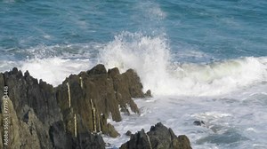Slow motion ocean waves swell and crash onto rocks and spray