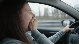 Side view of tired young woman yawning while driving car. Scene shows...