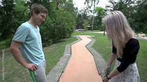 Girl swings golf club on mini golf club partner watching