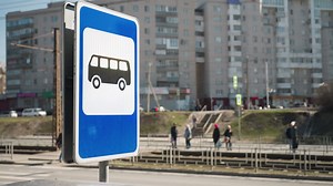 Close view of a bus stop sign in an urban setting with pedestrians walking in the background, while some persons are just standing | Premium Stock Video Footage