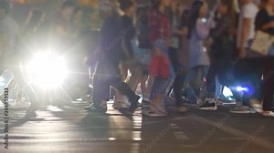 Crowd of people crossing street at a crosswalk in the evening. Cars with lights on standing in background. UHD Stock Video