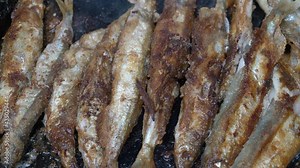 View of cooking frying capelin fish in iron pan. Broiled caplin fish - popular Korean cuisine where entire small fish, from head to tail, roe and bones can be enjoyed as an appetizer or garnish.