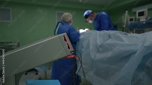 Close-up cautery machine with blurred plastic surgeon and nurse operating patient at background. Caucasian doctor and assistant stitching dissection in slow motion in medical clinic indoors