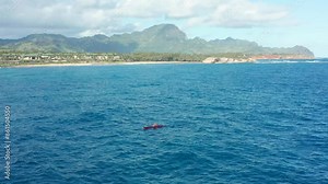 Hawaiian single outrigger canoe rowing on blue ocean in Hawaii. Aerial drone rotating shot exercising person in outrigger paddling boat. Coastline of Kauai island