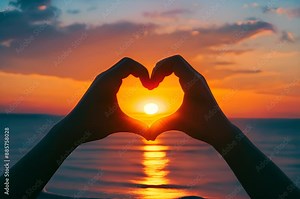 Sunset over sea, with sun perfectly positioned in the center of a silhouette of hands forming a heart shape, gently reflects on the water's surface, creating a romantic and peaceful atmosphere.