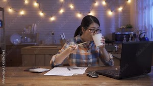 japanese female working at laptop computer eats instant ramen noodles late in evening. Woman typing on notebook keyboard chatting online overtime at night has fast dinner. concept unhealthy junk food