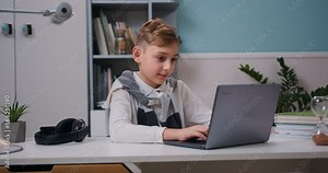 Boy using a laptop for studying, watching online lectures, workshops and master classes. Smart young boy attending online class on laptop computer in modern room at home.