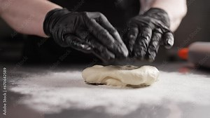 A man kneads dough in a pastry shop. Rolling out dough, close-up of a chef wearing gloves.