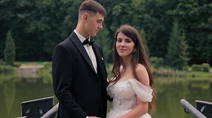 Romantic couple posing by serene lake surrounded by lush green nature, Bride and groom holding hands and sharing a romantic moment near a calm lake and forest.