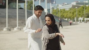 Young muslim couple performing traditional dance on sunny day. Arabic man in white gown and beautiful woman in hijab practicing dance moves outside, moving to music together. Ethnicity concept.