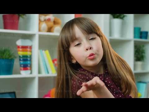 Cute little girl blowing kisses at the camera in kids room. White shelves with toys background