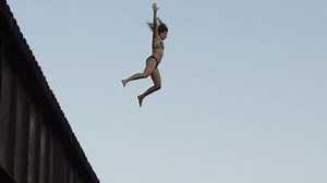 Young woman jumping off of a bridge into the water summer splash swimming