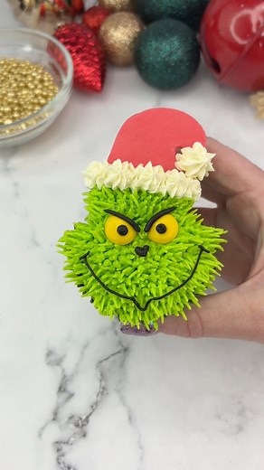 GRINCHMAS 💚❤️ He’s my most popular cupcake to date, so I wanted to remake him for you 💚❤️ #mrgrinch💚 Use foil balls to shape the cupcakes before baking.❤️ Pipe his fur using green buttercream and piping tip 233.💚 Chop the top off two yellow M&Ms and add them for the eyes. ❤️ Use a small round piping tip and black buttercream to add the face details.💚 I made his hat from red fondant and let it firm up before adding it. If needed, secure it with a cocktail stick until the buttercream sets. ❤️