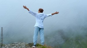 Woman stands atop a mountain, raising arms in the air and embracing the freedom of nature. The breathtaking view and serene surroundings evoke feelings of joy and tranquility