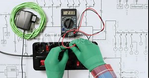 Technician tests socket extension with multimeter and plugs device on electrical schematic diagram upper view. Electrician controls network tense