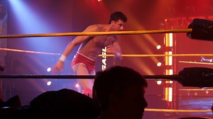 Two wrestlers engaged in a fast-paced move inside a brightly lit wrestling ring, with an intense atmosphere created by dramatic stage lighting. Surrounded by a captivated audience | Premium Stock Video Footage