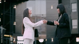 Meeting of two business women. Two young women dressed in business suits are shaking hands when meeting on a city street.